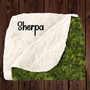 May include: A soft, white sherpa blanket with a green mossy pattern. The blanket has the word "Sherpa" printed on the white side.