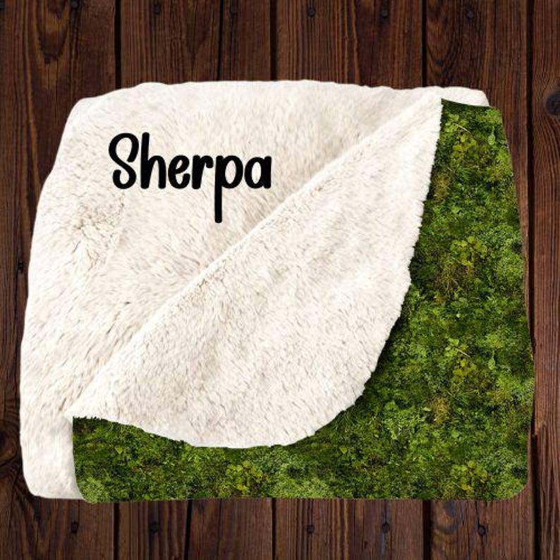 May include: A soft, white sherpa blanket with a green mossy pattern. The blanket has the word "Sherpa" printed on the white side.