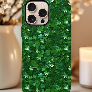 May include: Green phone case covered in a pattern of glittery shamrocks. The case has a black border and a camera cutout. The shamrocks are in various shades of green and white, creating a textured appearance.