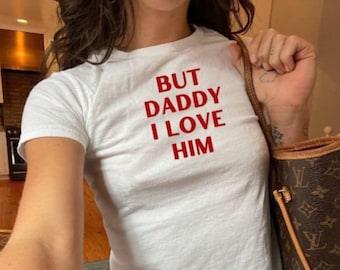 Puede incluir: Camiseta blanca con texto rojo que dice "But Daddy I Love Him".
