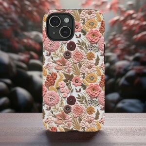 May include: A floral phone case featuring a detailed pattern of embossed flowers in shades of pink, peach, and brown. The case has a white background and a raised texture, giving it a 3D appearance. The phone case is on a wooden surface.