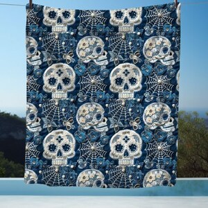 May include: A blue and white throw blanket with a repeating pattern of sugar skulls, flowers, and spiderwebs.