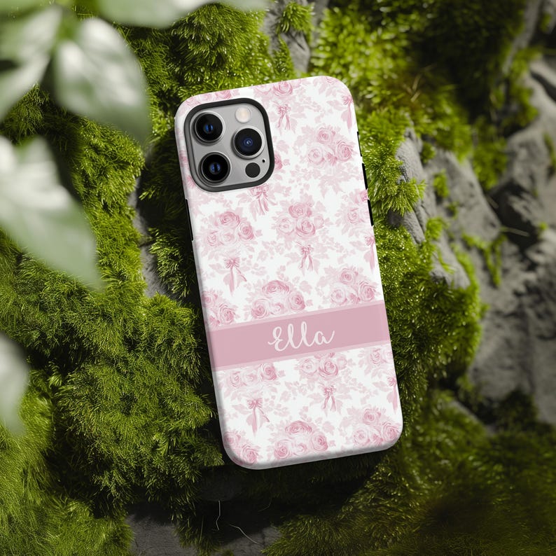 Op de afbeelding: Een witte telefoonhoes met een roze bloemenpatroon en de naam "Ella" gedrukt op een roze streep.