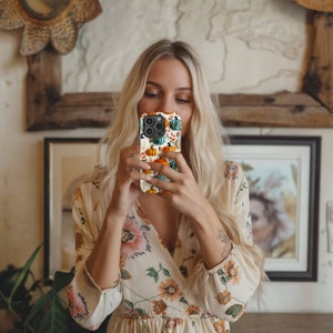 Peut inclure: Une coque de t&eacute;l&eacute;phone iPhone blanche avec un motif de citrouilles color&eacute;es. La coque pr&eacute;sente une vari&eacute;t&eacute; de citrouilles orange, vertes et bleues avec des tiges et des feuilles blanches.