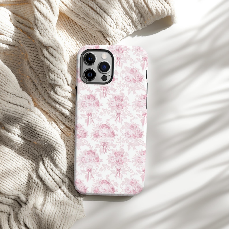 Op de afbeelding: Een witte telefoonhoes met een roze bloemenpatroon. De hoes heeft een uitsparing voor de cameralens en een zwarte rand.