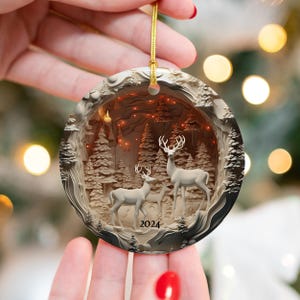 May include: White ceramic Christmas ornament with a 3D carved design of a winter forest scene with two white deer and the year 2024.