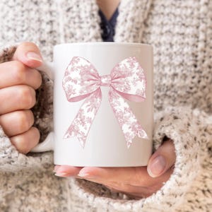 May include: White ceramic mug with a pink floral patterned bow design.