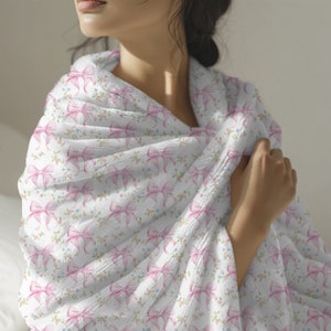 May include: A white throw blanket with a pink bow pattern. The blanket is soft and cozy, perfect for snuggling up on the couch.