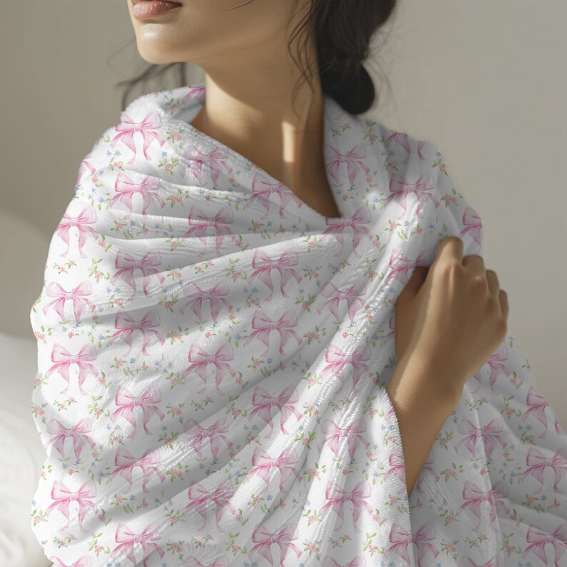 May include: A white throw blanket with a pink bow pattern. The blanket is soft and cozy, perfect for snuggling up on the couch.