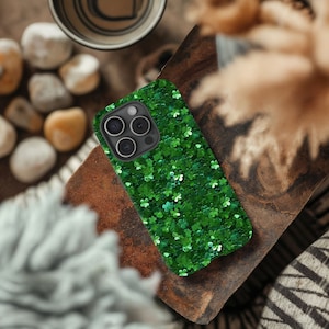 Könnte beinhalten: Eine grüne Glitzer-Handyhülle mit Kleeblatt-Design. Die Hülle ist für ein iPhone mit einer Dreifach-Kamera konzipiert.