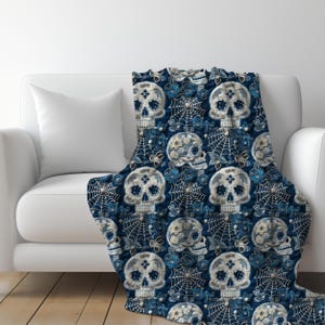 May include: A blue throw blanket with a repeating pattern of white sugar skulls with floral details and spiderwebs.