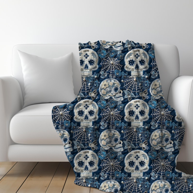 May include: A blue throw blanket with a repeating pattern of white sugar skulls with floral details and spiderwebs.