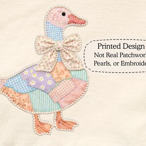 May include: A whimsical goose design with a patchwork pattern in pastel colors, including pink, blue, and lavender. The goose has a floral bow and is outlined with faux pearls. The text reads "Printed Design Not Real Patchwork, Pearls, or Embroidery."
