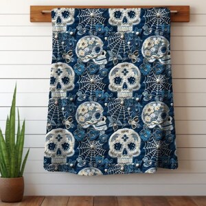 May include: Blue throw blanket with a repeating pattern of white sugar skulls with floral details and spiderwebs.