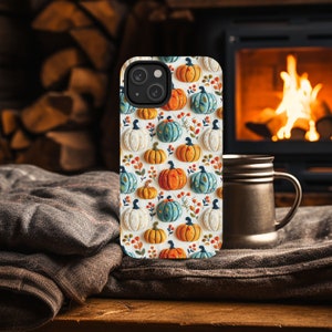 Peut inclure: Une coque de t&eacute;l&eacute;phone iPhone blanche avec un motif de citrouilles color&eacute;es. La coque a un d&eacute;coupage pour l'objectif de l'appareil photo et un fond blanc.