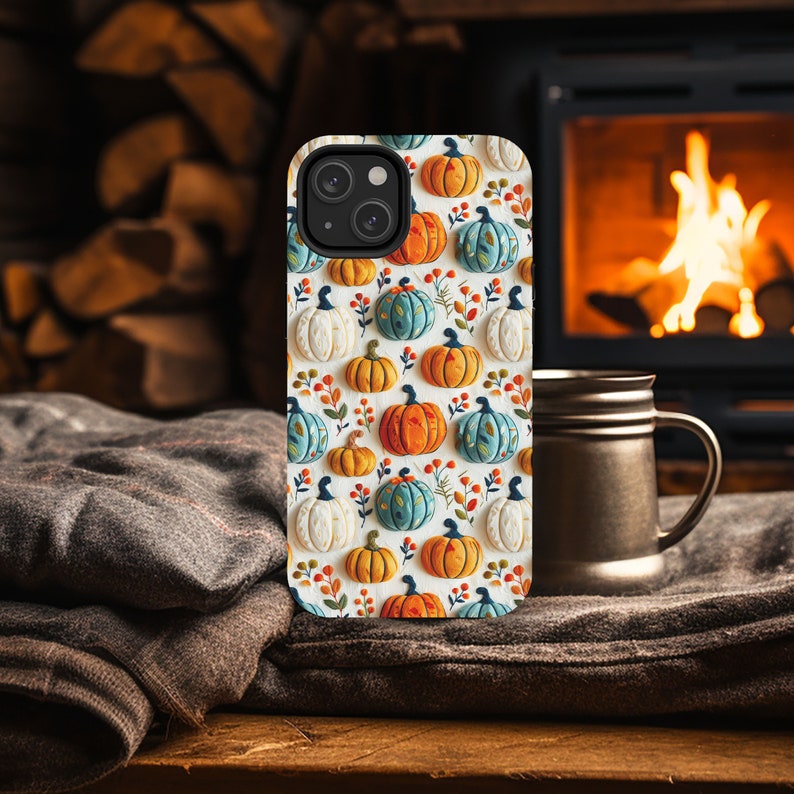Peut inclure: Une coque de t&eacute;l&eacute;phone iPhone blanche avec un motif de citrouilles color&eacute;es. La coque a un d&eacute;coupage pour l'objectif de l'appareil photo et un fond blanc.