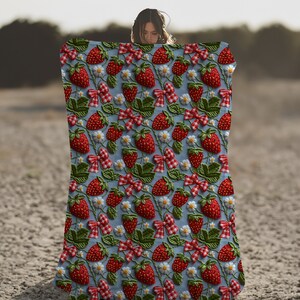 May include: A blue and white throw blanket with a repeating pattern of embroidered red strawberries, green leaves, and white flowers.