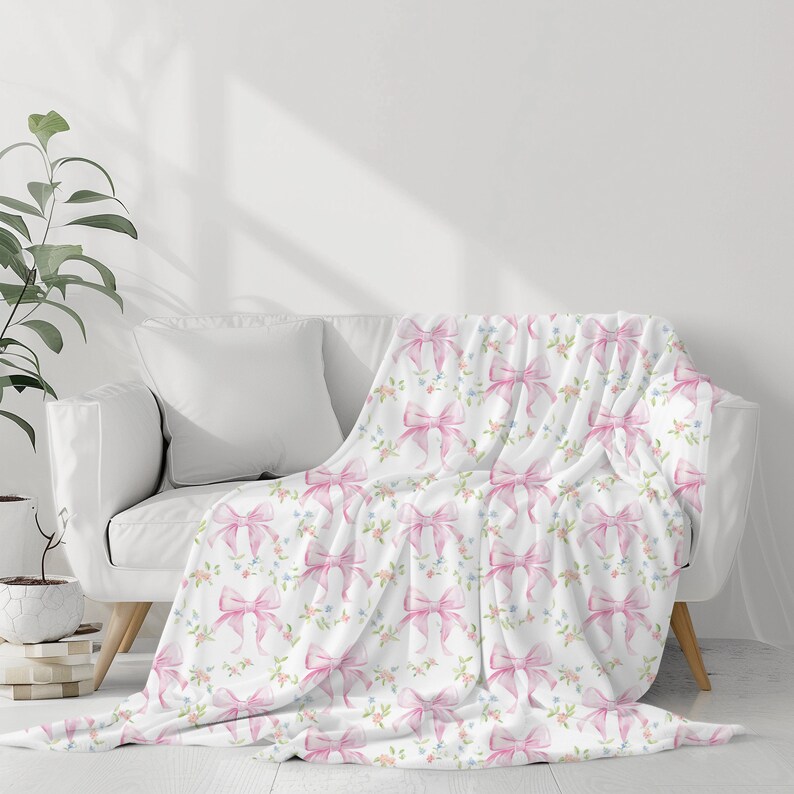 May include: A white throw blanket with a pink bow and floral pattern. The blanket is draped over a white couch.