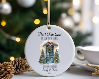 May include: White ceramic Christmas ornament with a watercolor illustration of a blue front door with a wreath and greenery. The text reads "First Christmas in our new home 122 Main Street Emily & Chase 2023".