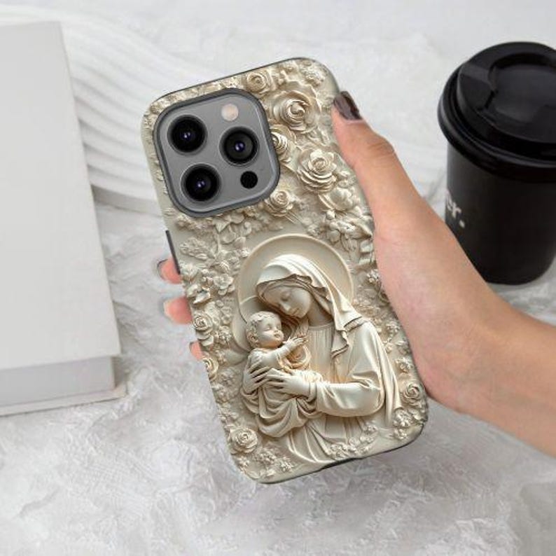 May include: A white iPhone case with a carved design of a mother and child. The design is in a relief style and features intricate details. The case is compatible with iPhone models with a triple camera lens.