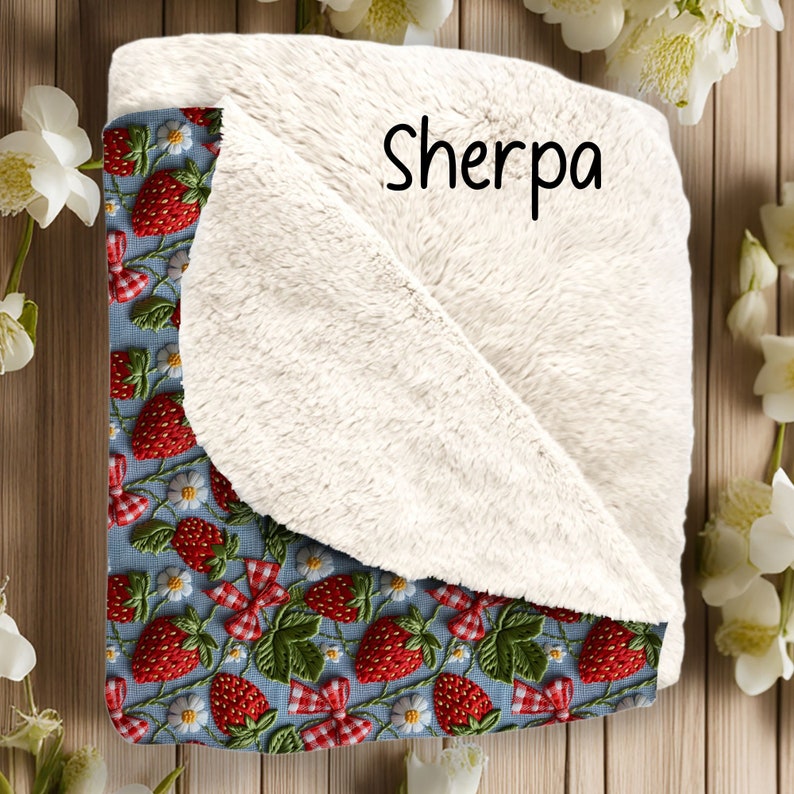 May include: A blue and white throw blanket with a sherpa lining. The blanket features a repeating pattern of embroidered strawberries and flowers. The text "Sherpa" is printed on the blanket.