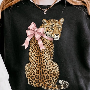 Op de afbeelding: Zwart sweatshirt met een illustratie van een luipaard met een roze strik. De luipaard heeft een gevlekte vacht en zit rechtop. Het sweatshirt is een casual stijl, geschikt voor dagelijks gebruik.