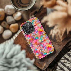 May include: A colorful phone case with a pattern of multi-colored stars. The case is designed for an iPhone 14 Pro Max.