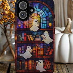 May include: A phone case featuring a stained-glass design with ghosts reading books on a bookshelf. The case has a dark background with colorful books and ghosts, perfect for Halloween or book lovers.