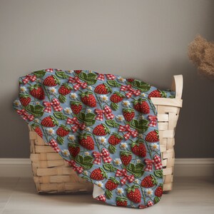 May include: A woven basket filled with a blue fabric featuring a repeating pattern of red strawberries and white flowers. The fabric has a light blue background with a white border.