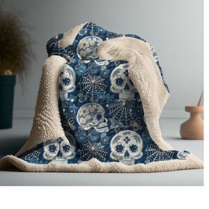 May include: A soft, blue and white throw blanket with a sugar skull pattern. The blanket is made of a plush, sherpa material and is perfect for cuddling up on the couch.