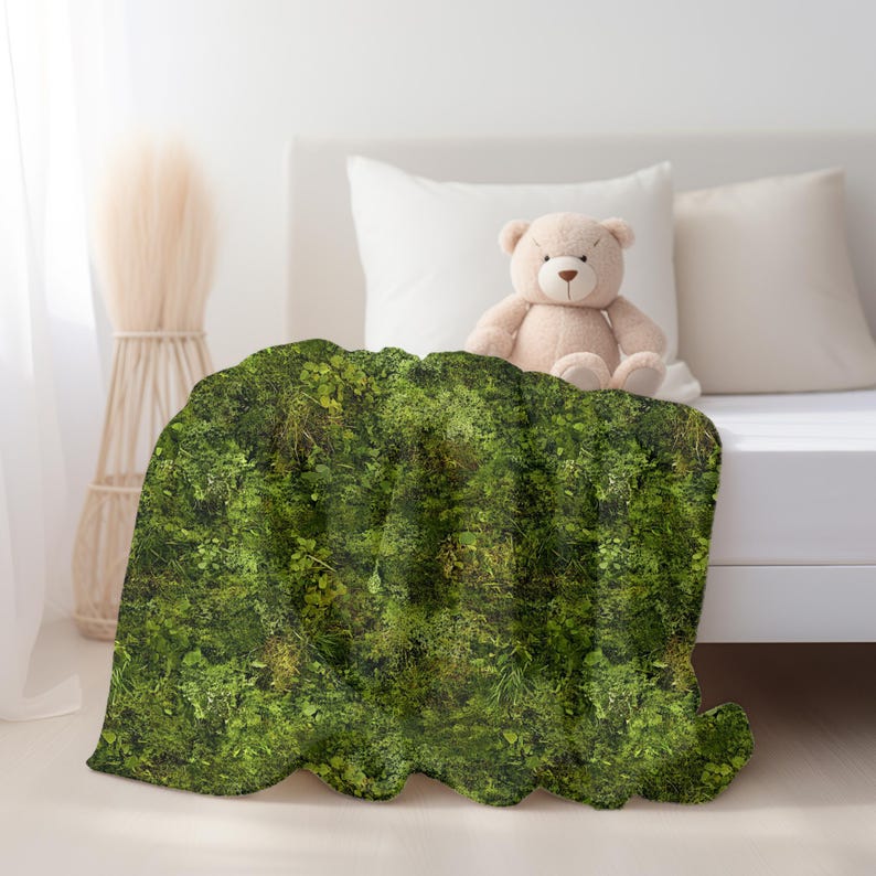 May include: A green mossy patterned throw blanket with a teddy bear sitting on a white bed.