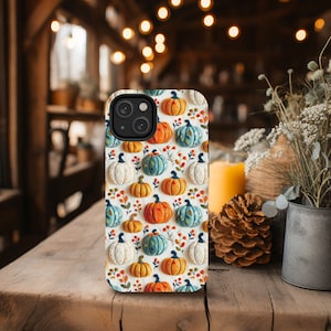 Peut inclure: Une coque de t&eacute;l&eacute;phone iPhone blanche avec un motif de citrouilles color&eacute;es, de feuilles et de vignes. La coque a un d&eacute;coupage pour l'appareil photo et un fond blanc.
