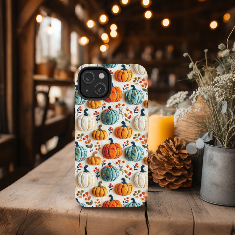 Peut inclure: Une coque de t&eacute;l&eacute;phone iPhone blanche avec un motif de citrouilles color&eacute;es, de feuilles et de vignes. La coque a un d&eacute;coupage pour l'appareil photo et un fond blanc.