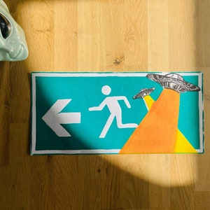 Linocut “EXIT” wall poster of an emergency exit sign with UFOs, hand-printed and limited