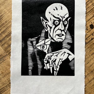 Schwarz/Weiss Linoldruck. Motiv: Nosferatu mit einem Glas Martiniin der Hand. Nosferatu trinkt diesen natürlich mit einem aufgespiessten Augapfel, anstelle einer klassischen Olive :). Der Druck ist handgezeichnet, handgedruckt und signiert.