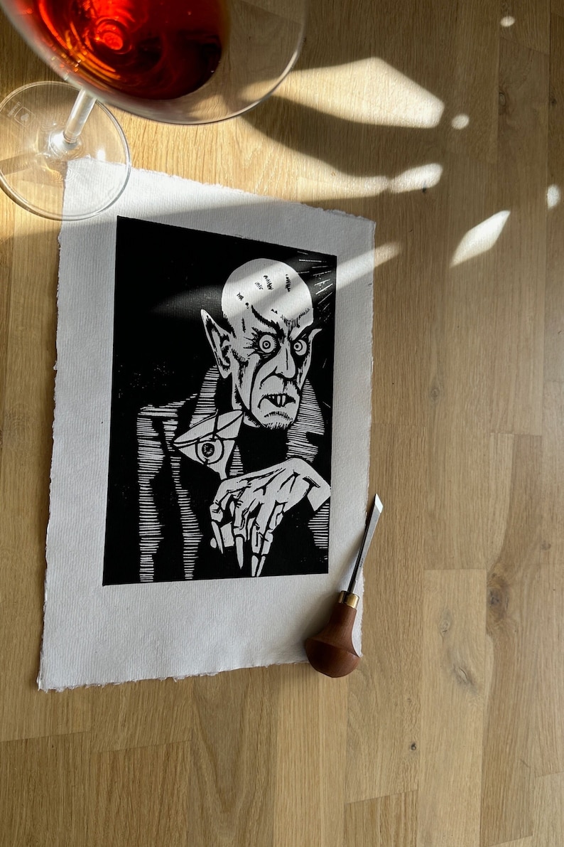 Schwarz/Weiss Linoldruck. Motiv: Nosferatu mit einem Glas Martiniin der Hand. Nosferatu trinkt diesen natürlich mit einem aufgespiessten Augapfel, anstelle einer klassischen Olive :). Der Druck ist handgezeichnet, handgedruckt und signiert.