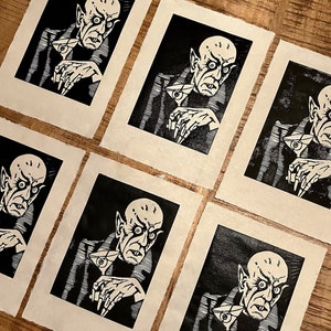 Schwarz/Weiss Linoldruck. Motiv: Nosferatu mit einem Glas Martiniin der Hand. Nosferatu trinkt diesen natürlich mit einem aufgespiessten Augapfel, anstelle einer klassischen Olive :). Der Druck ist handgezeichnet, handgedruckt und signiert.