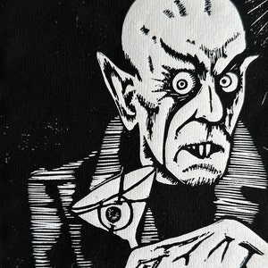 Schwarz/Weiss Linoldruck. Motiv: Nosferatu mit einem Glas Martiniin der Hand. Nosferatu trinkt diesen natürlich mit einem aufgespiessten Augapfel, anstelle einer klassischen Olive :). Der Druck ist handgezeichnet, handgedruckt und signiert.