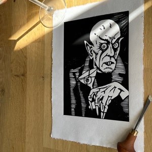 Schwarz/Weiss Linoldruck. Motiv: Nosferatu mit einem Glas Martiniin der Hand. Nosferatu trinkt diesen natürlich mit einem aufgespiessten Augapfel, anstelle einer klassischen Olive :). Der Druck ist handgezeichnet, handgedruckt und signiert.