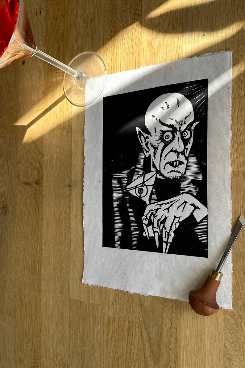 Schwarz/Weiss Linoldruck. Motiv: Nosferatu mit einem Glas Martiniin der Hand. Nosferatu trinkt diesen natürlich mit einem aufgespiessten Augapfel, anstelle einer klassischen Olive :). Der Druck ist handgezeichnet, handgedruckt und signiert.