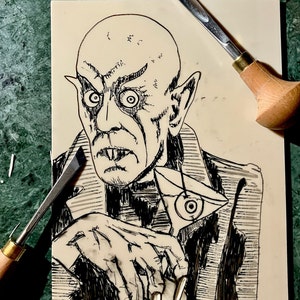 Schwarz/Weiss Linoldruck. Motiv: Nosferatu mit einem Glas Martiniin der Hand. Nosferatu trinkt diesen natürlich mit einem aufgespiessten Augapfel, anstelle einer klassischen Olive :). Der Druck ist handgezeichnet, handgedruckt und signiert.