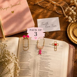 Puede incluir: Un juego de tres marcapáginas de metal dorado con forma de clip. Uno tiene dos cuentas de color rosa brillante, otro un dije de lazo rosa con cuentas de color rosa claro y el tercero tiene forma de cruz con un pequeño corazón rojo. Pack of 3.