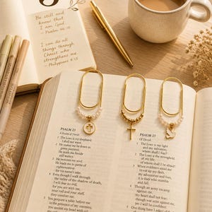 Puede incluir: Un paquete de tres marcapáginas de metal dorado con forma de clip sobre un libro abierto. Cada marcapáginas tiene un dije colgante: uno con una cruz blanca, otro con una cruz dorada y otro con una paloma blanca, con pequeñas cuentas.