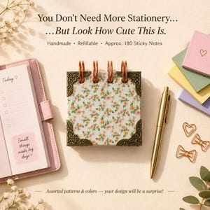 May include: A square refillable sticky note pad with a floral pattern, copper-colored spiral binding, and ornate metal corner protectors. Includes a pink planner, a gold pen, and heart-shaped paper clips. Text reads: You Don't Need More Stationery... But Look How Cute This Is. Handmade • Refillable • Approx. 180 Sticky Notes.