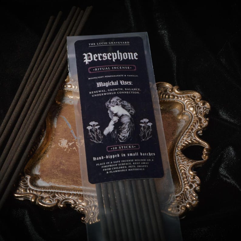 May include: A packet of Persephone ritual incense, with the text "The Lucid Graveyard". The package contains 10 sticks and lists "Moonlight Pomegranate & Vanilla" as the scent. The package is on a gold-coloured decorative tray.
