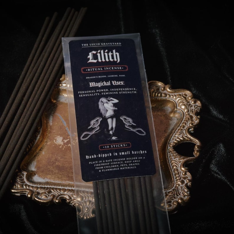 May include: A package of "Lilith" ritual incense sticks with a black and white label. The label includes text about the incense's uses and ingredients. The incense is displayed on a decorative gold-colored tray.