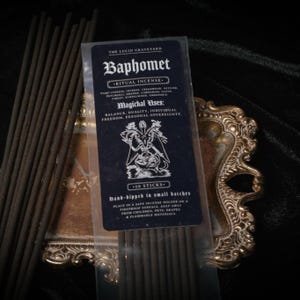 May include: A package of Baphomet ritual incense with 10 sticks, featuring a dark blue label with white text and an illustration. The label lists ingredients and magical uses. Incense sticks are brown, and the package rests on a decorative gold-colored tray.