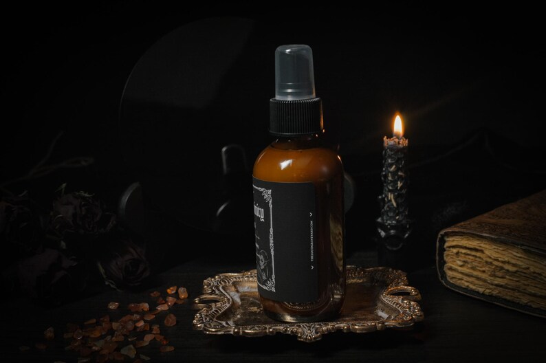 Puede incluir: Una botella de vidrio marr&oacute;n con una etiqueta negra y una boquilla de pulverizaci&oacute;n transparente. La botella est&aacute; sentada en una bandeja de metal dorado. Una vela negra est&aacute; ardiendo en el fondo.