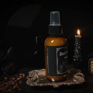 Puede incluir: Una botella de vidrio marr&oacute;n con una etiqueta negra que dice "Dark Desire" y "Midnight" en una fuente g&oacute;tica. La botella est&aacute; sentada en una bandeja dorada con una vela encendida en el fondo.