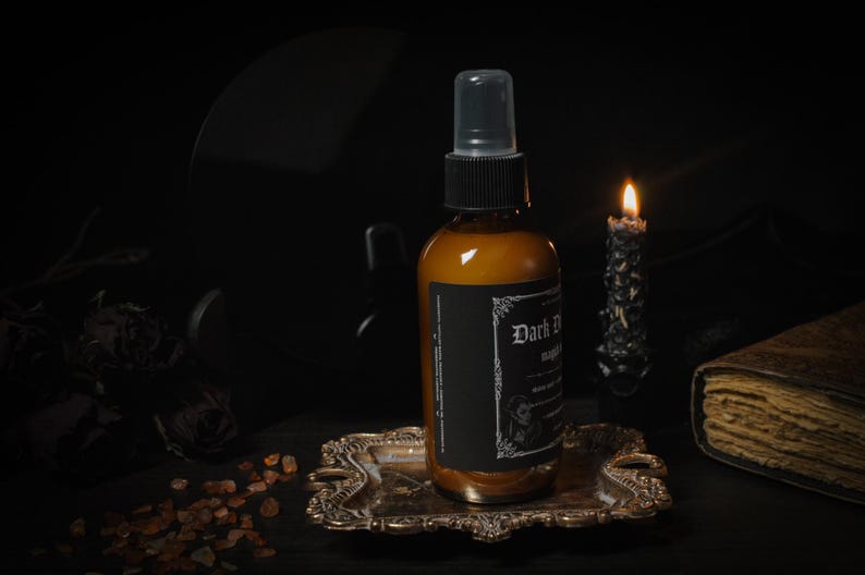 Puede incluir: Una botella de vidrio marr&oacute;n con una etiqueta negra que dice "Dark Desire" y "Midnight" en una fuente g&oacute;tica. La botella est&aacute; sentada en una bandeja dorada con una vela encendida en el fondo.